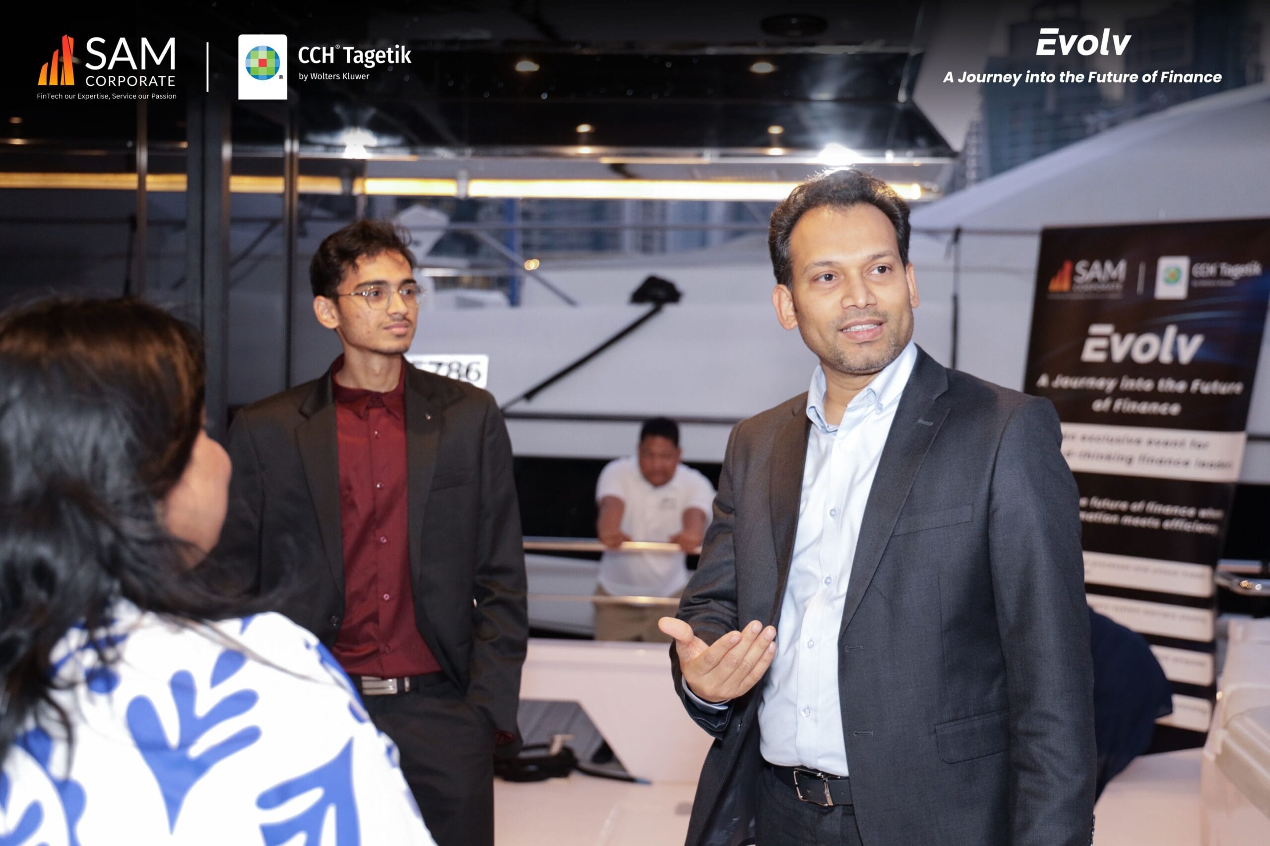 An executive speaking to attendees near the branded signage for the Evolv event, co-hosted by SAM Corporate and CCH Tagetik.