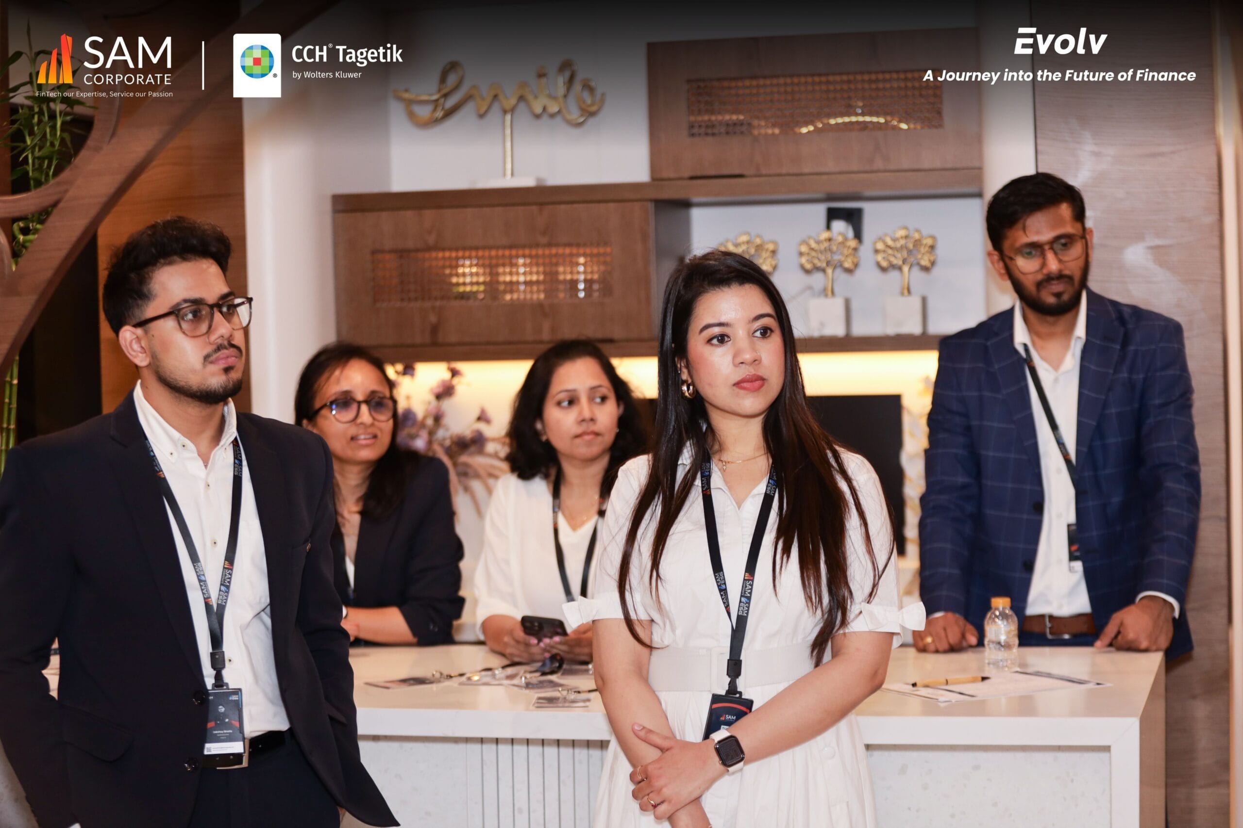 Group of five finance professionals standing attentively at the reception area of the Evolv summit by SAM Corporate and CCH Tagetik.