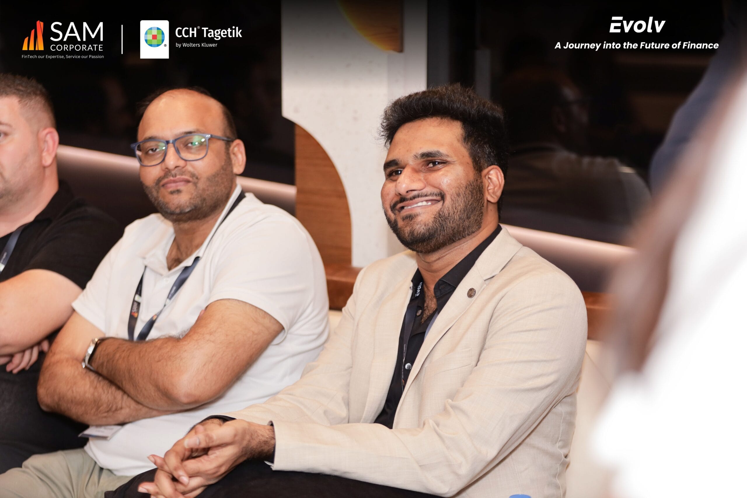 Two smiling finance professionals and attendees listening to a presentation at the Evolv event by SAM Corporate and CCH Tagetik.