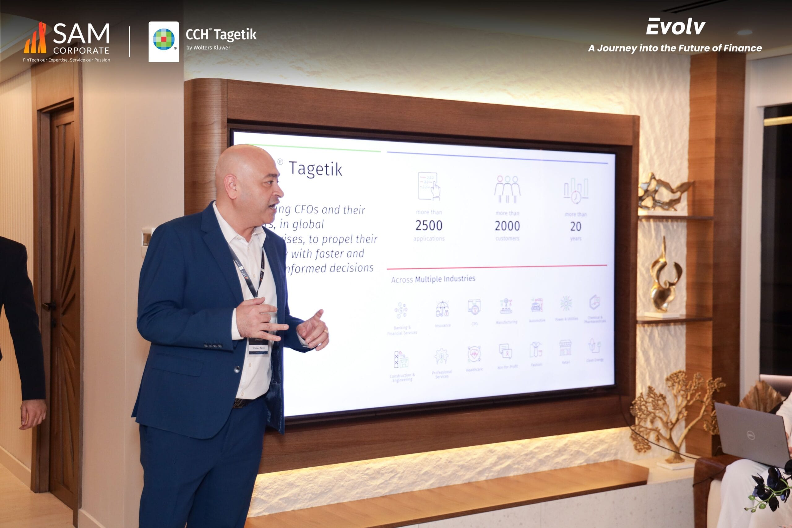 Presenter speaking next to a screen showing CCH Tagetik statistics at the Evolv summit.