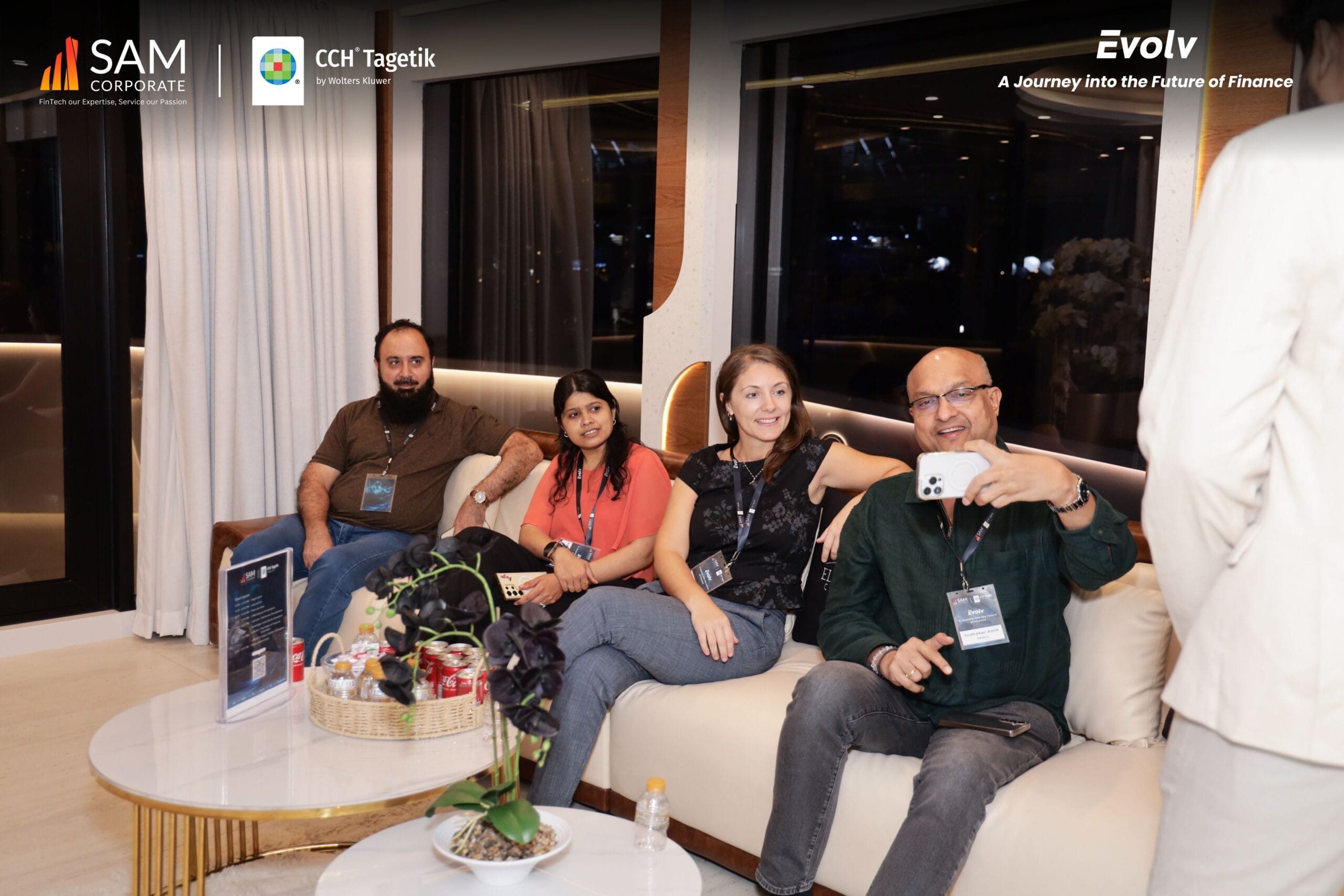 A group of four attendees taking a photo together in the lounge area of the Evolv event, sponsored by SAM Corporate and CCH Tagetik.