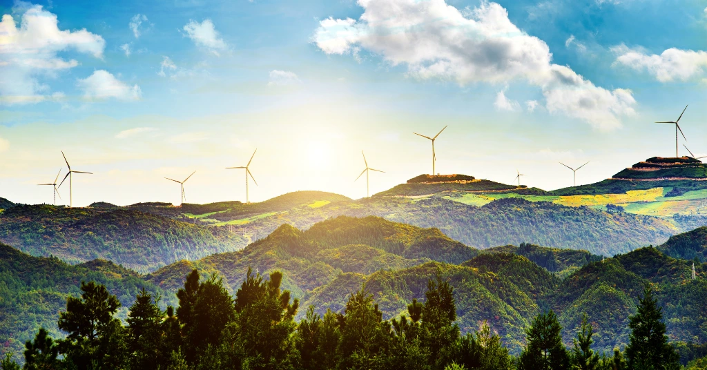 A scenic landscape of rolling green hills at sunset featuring multiple wind turbines, representing renewable energy and climate transition initiatives.