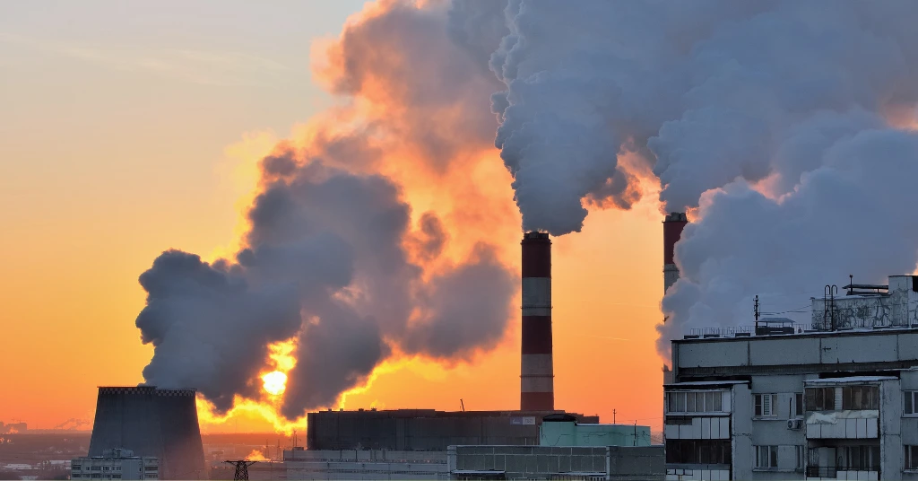 Thick smoke rising from power plant chimneys against a sunset sky highlighting the impact of industrial emissions.