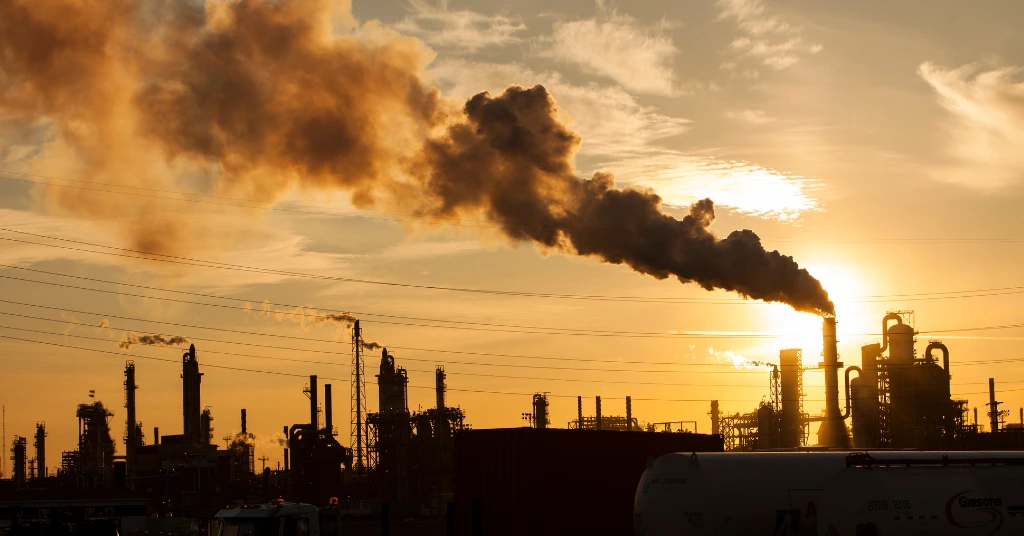 Industrial factory silhouette with smoke emissions during sunset.