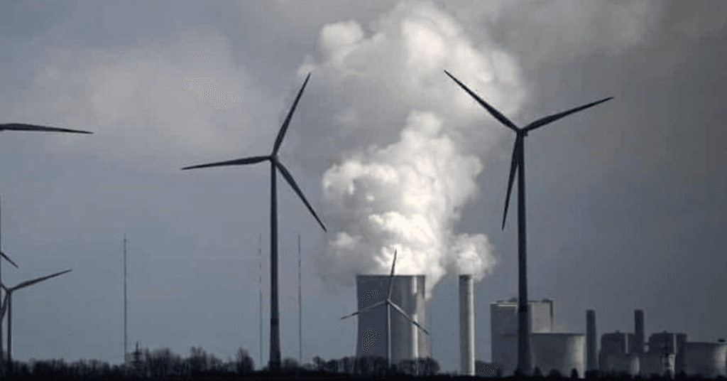 Wind turbines in the foreground with industrial cooling towers emitting steam in the background representing energy transition.